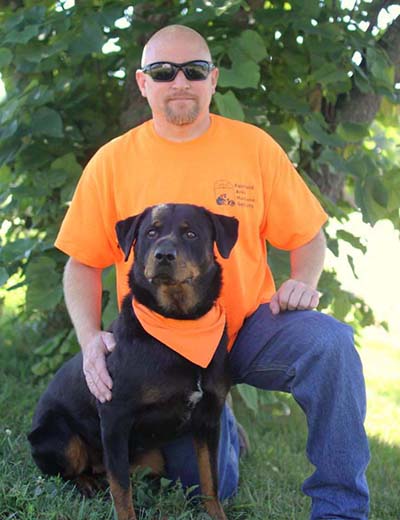 Trainer Dave kneeling beside a Rottweiler